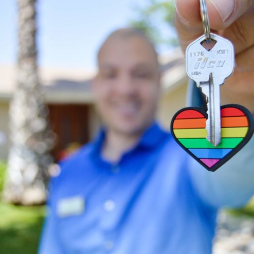 man holding up keys to a new house with a rainbow loveheart keyring