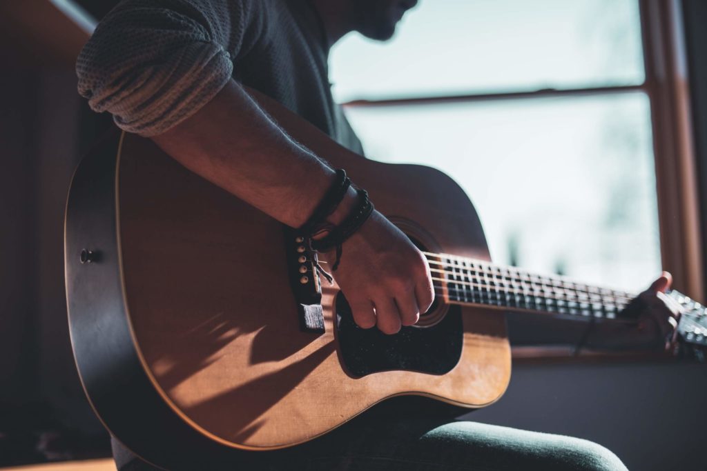 man wearing leather bracelets playing guitar near a window