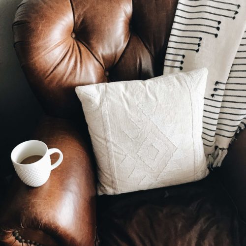 brown leather couch with coffee mug white pillow and blanket