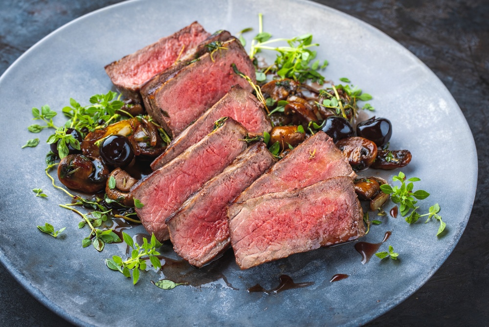 A nice beef roast on a plate garnished and topped with gravy and mushrooms.