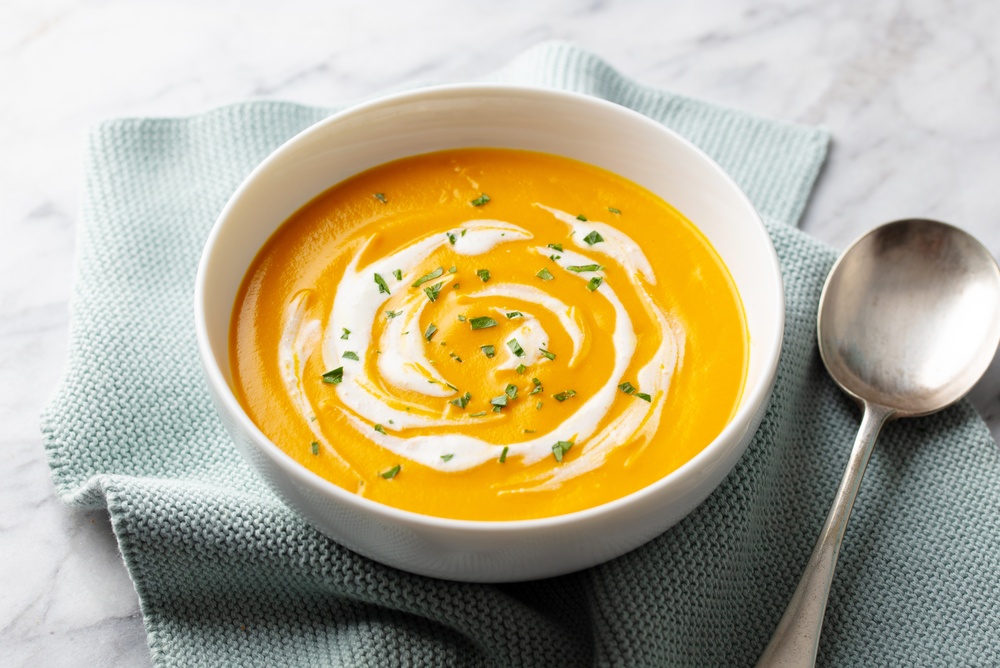 A delicious serving of pumpkin soup ready to eat of a kitchen bench.