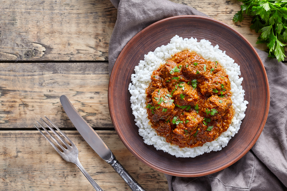 Indian madras curry served on top of a bed of rice ready to serve on a wooden table.