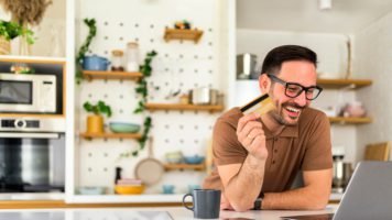 Man on his laptop in the kitchen learning money saving tips from swoosh finance