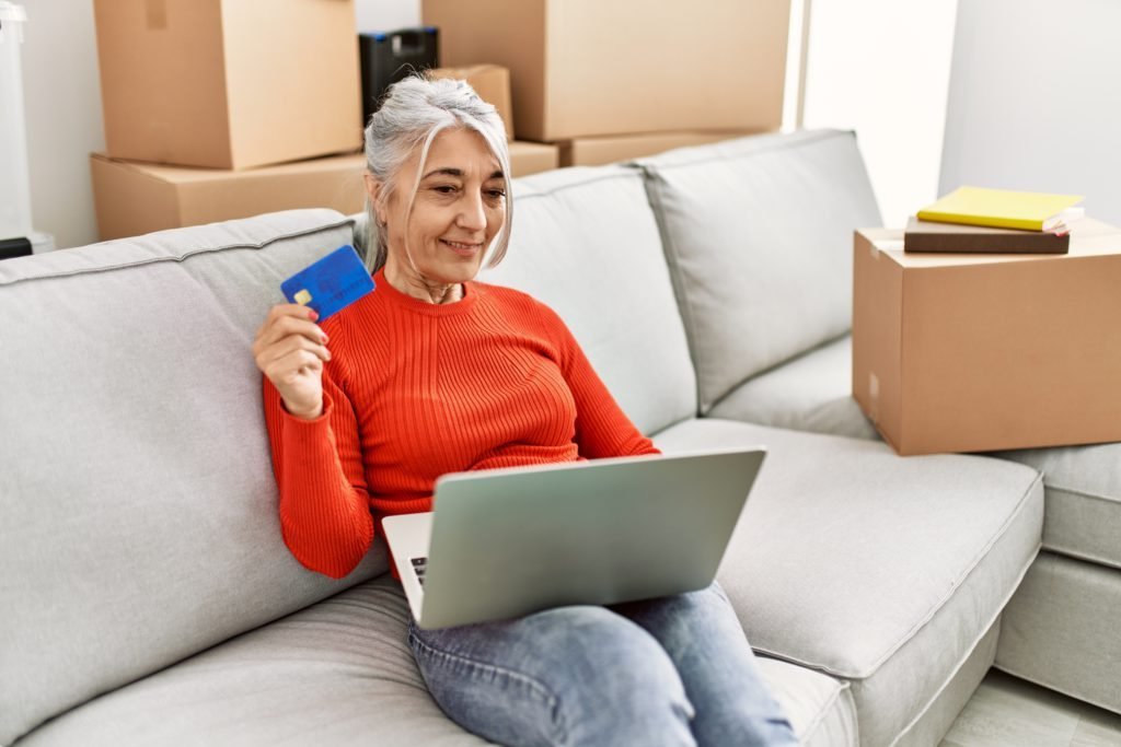 Older woman sitting on her couch with her laptop and credit card, learning how to start building a credit history | Swoosh Finance