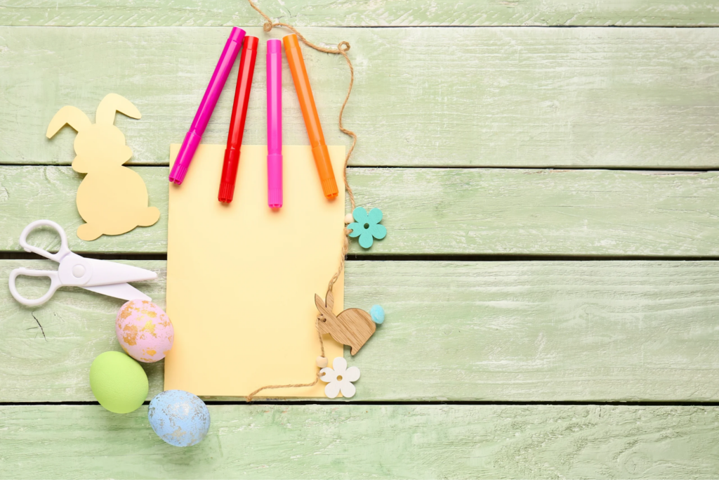 Easter craft supplies laid out with coloured pens, safety scissors, yellow paper and bunny cut-outs