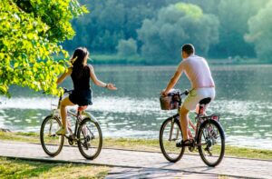 A couple bike riding in the park on a beautiful day in the summer time.