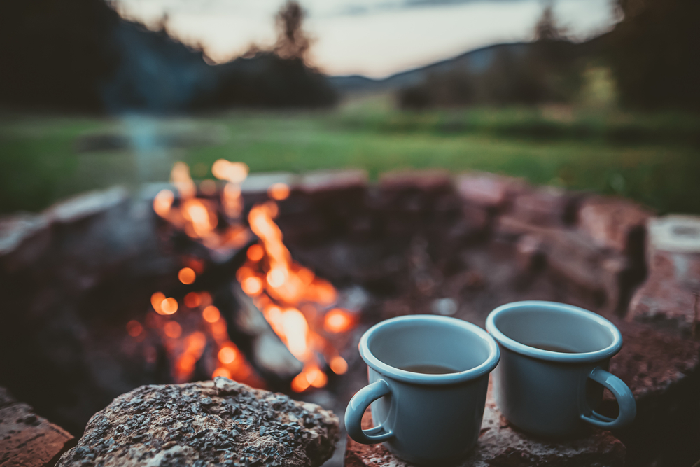 A campfire in the background and the focus on two hot chocolate mugs.