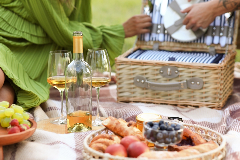 A beautiful picnic with fruits, crackers and wine is laid out on a picnic blanket.