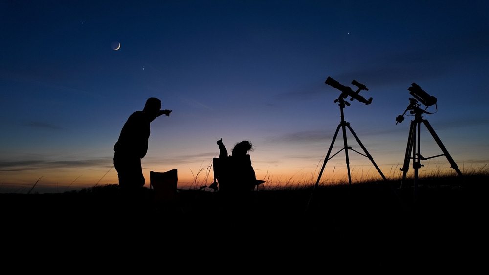 Two people on a date with telescopes stargazing at night.