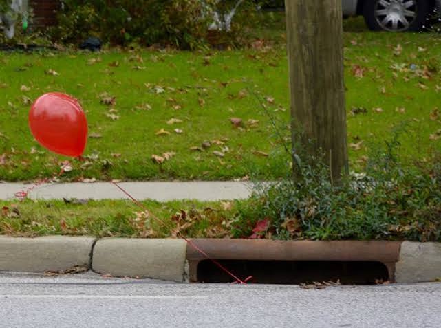 A red balloon peaking out of a drawn on a nice neighbourhood street.
