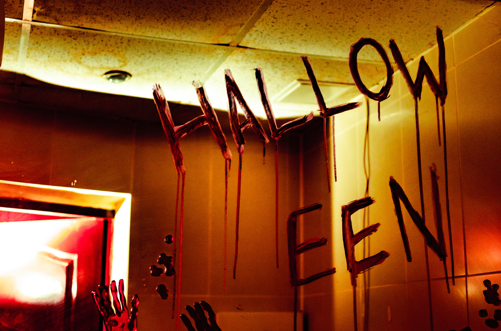 The word halloween written on a mirror in red paint that is dripping.