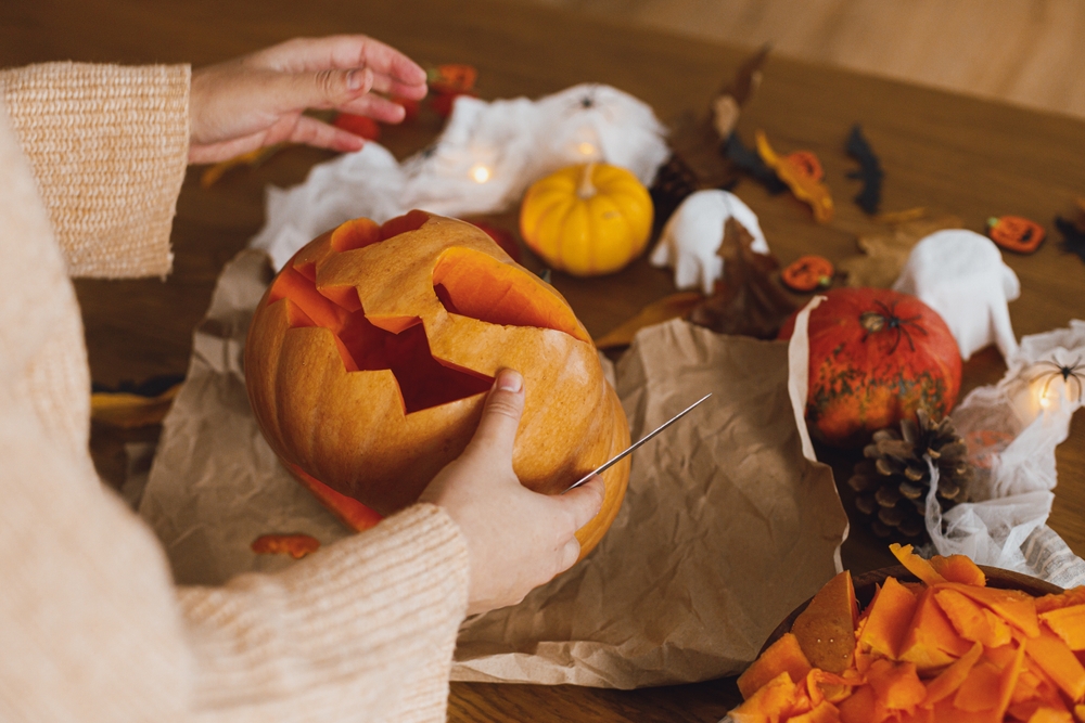 A lady carving out a face on a pumpkin.