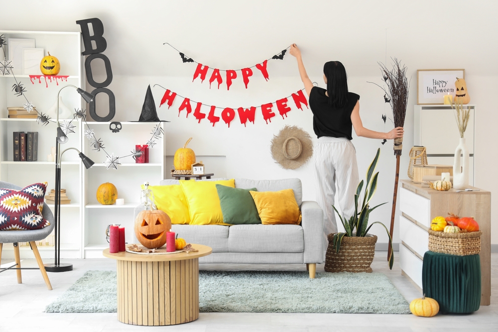 A lady decorating for Halloween and putting up a halloween banner in her living room.