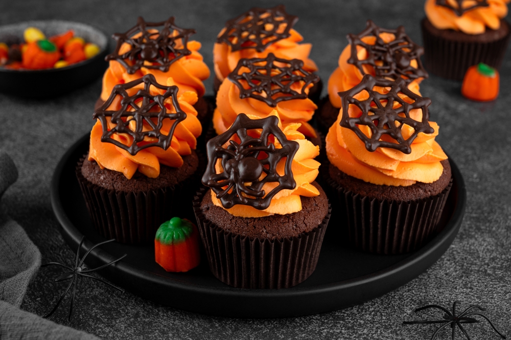 Chocolate cupcakes with orange icing and chocolate shapped spider webs on top.