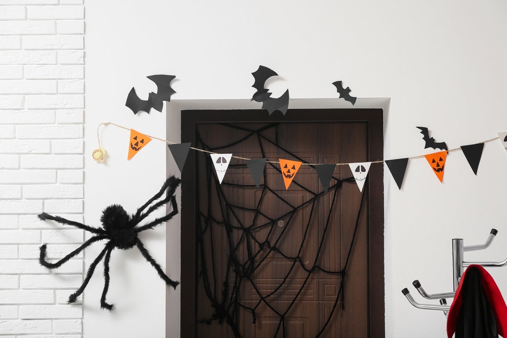 Halloween decorated door with spiders, garland and spooky paper cutouts.
