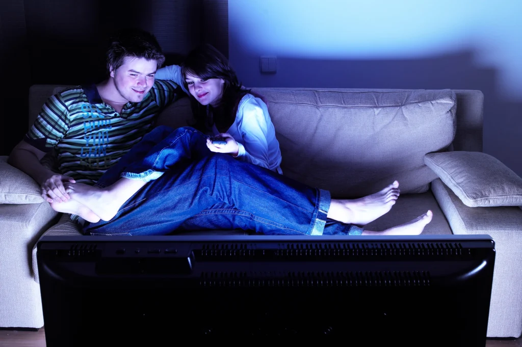 couple cuddling on couch watching free streaming service in the dark, lit up by TV screen