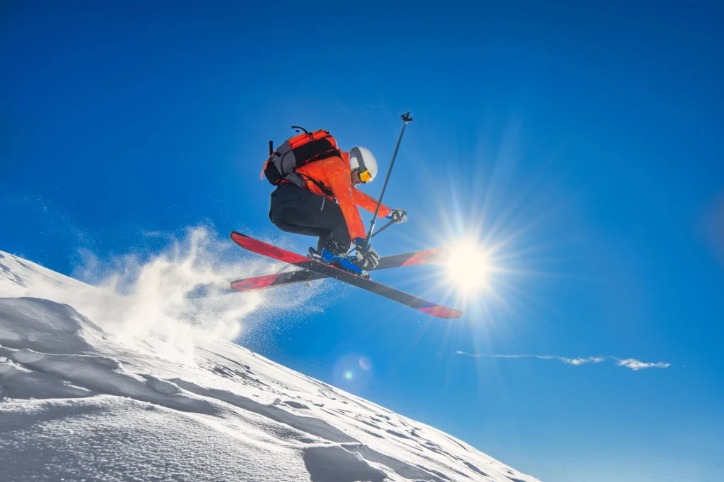 man ski jumping on snowy hill with sun shining in background