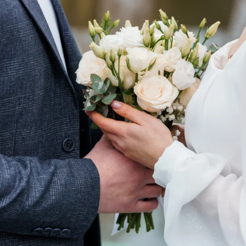 Close up of bride and groom's hands both holding flower bouquet at wedding | Are Wedding Loans a Good Idea?