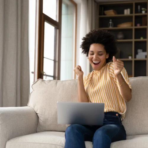 A woman grins and dances looking at her laptop, celebrating an instant approval loan