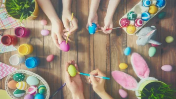 Close up of mum, dad, and child's hands painting easter eggs together at a table