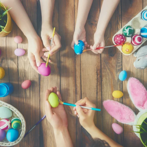 Close up of mum, dad, and child's hands painting easter eggs together at a table