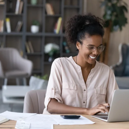 Smiling woman works on her laptop figuring out how to save money long term