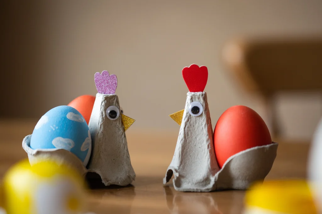 Two chickens made from cut out egg cartons, dyed eggs, and googly eyes