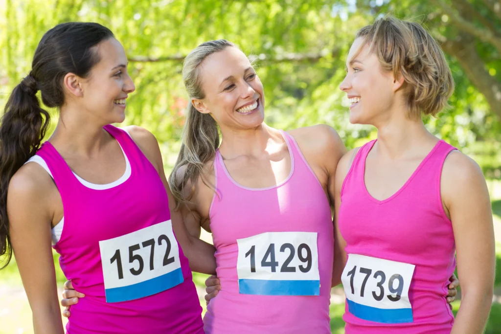 three woman posing together before Mother's Day running charity event in pink singlet tops and numbers taped on them