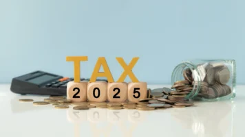 Dice that spell out 2025 with the word Tax on top. A jar of coins on one side, and a calculator on the other