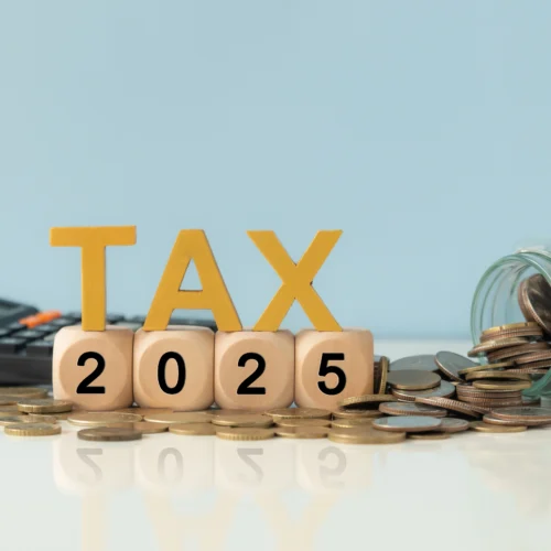Dice that spell out 2025 with the word Tax on top. A jar of coins on one side, and a calculator on the other