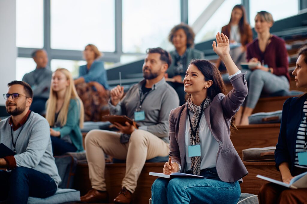 Woman in a lecture hall with her hand up, participating in a further studies class with other mature age students.