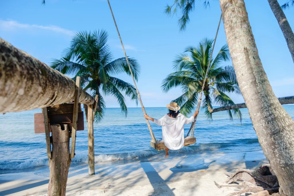 Woman on a swing connected to palm trees right in front of the beach on a tropical holiday location