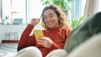 loans against cars; happy woman sitting on couch and using her phone | Swoosh Finance