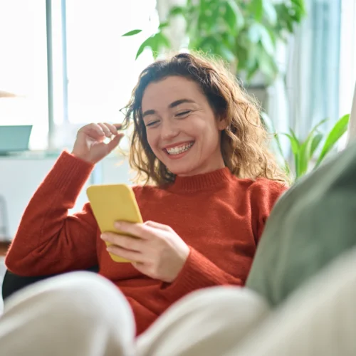 loans against cars; happy woman sitting on couch and using her phone | Swoosh Finance