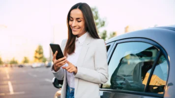 Woman standing next to her car smiles at her phone