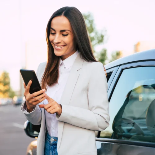Woman standing next to her car smiles at her phone