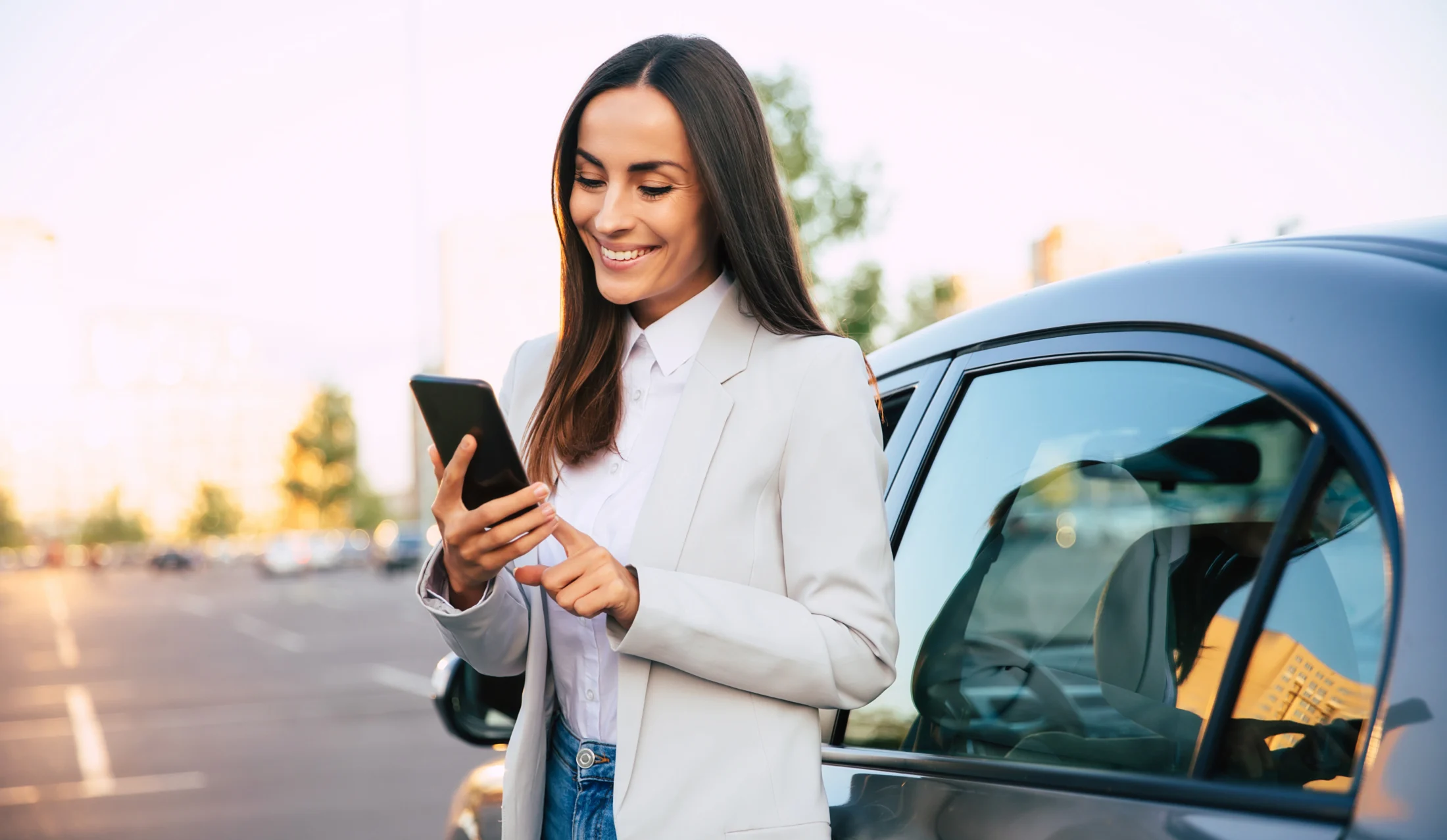 Woman standing next to her car smiles at her phone