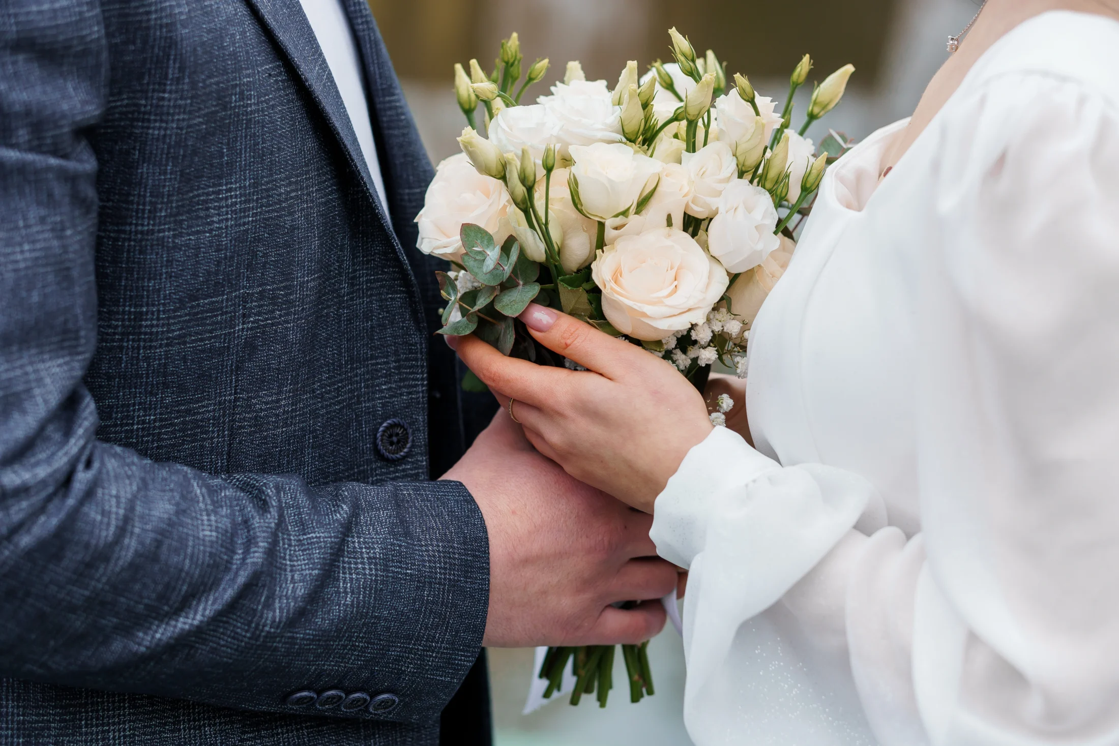 Close up of bride and groom's hands both holding flower bouquet at wedding