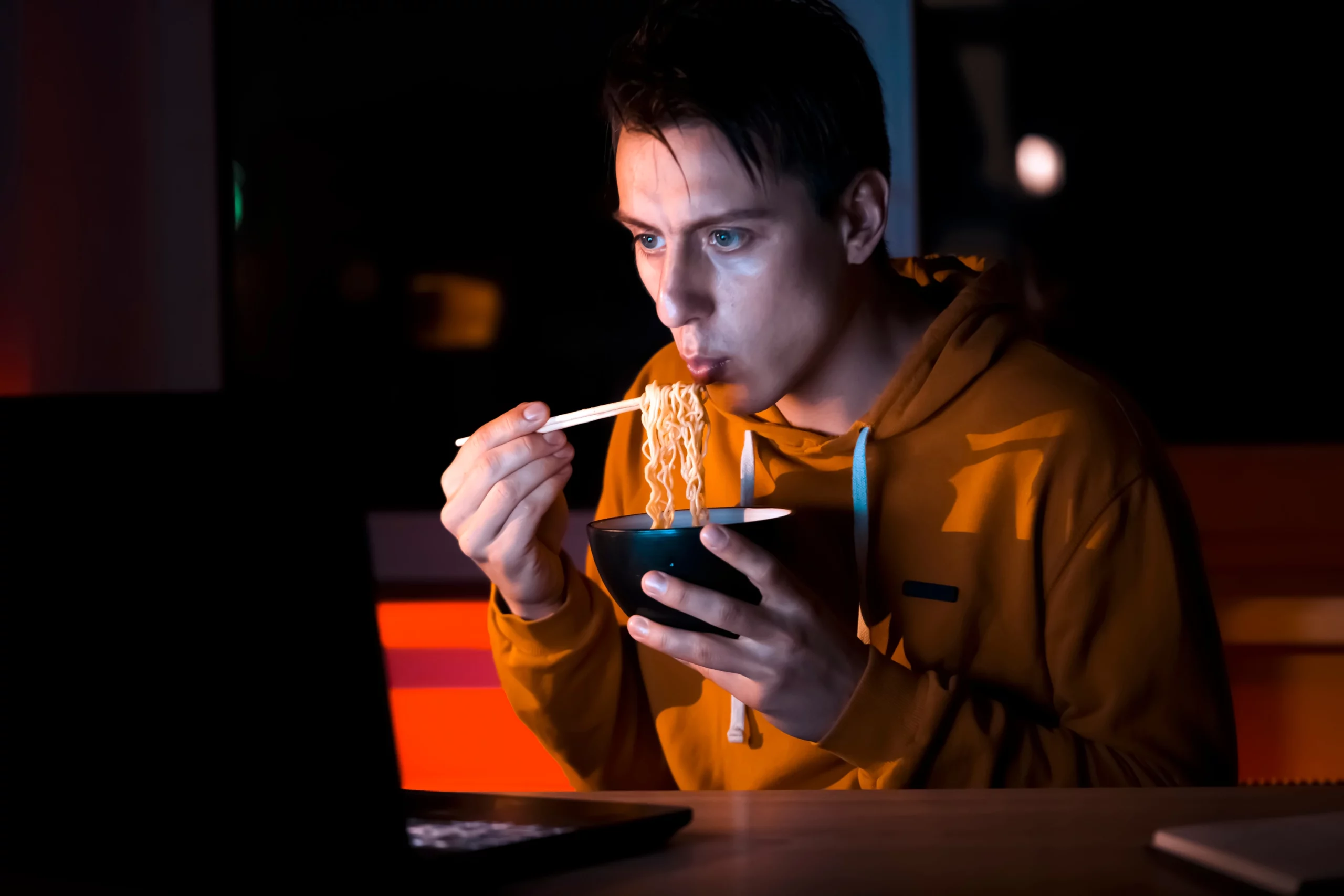 man watching a movie on his laptop while eating noodle soup with chopsticks