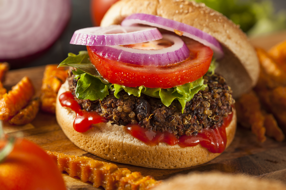 A delicious black bean and quinoa burger, topped with lettuce, tomato, and red onion slices, drizzled with ketchup. Crinkle-cut fries surround the burger.