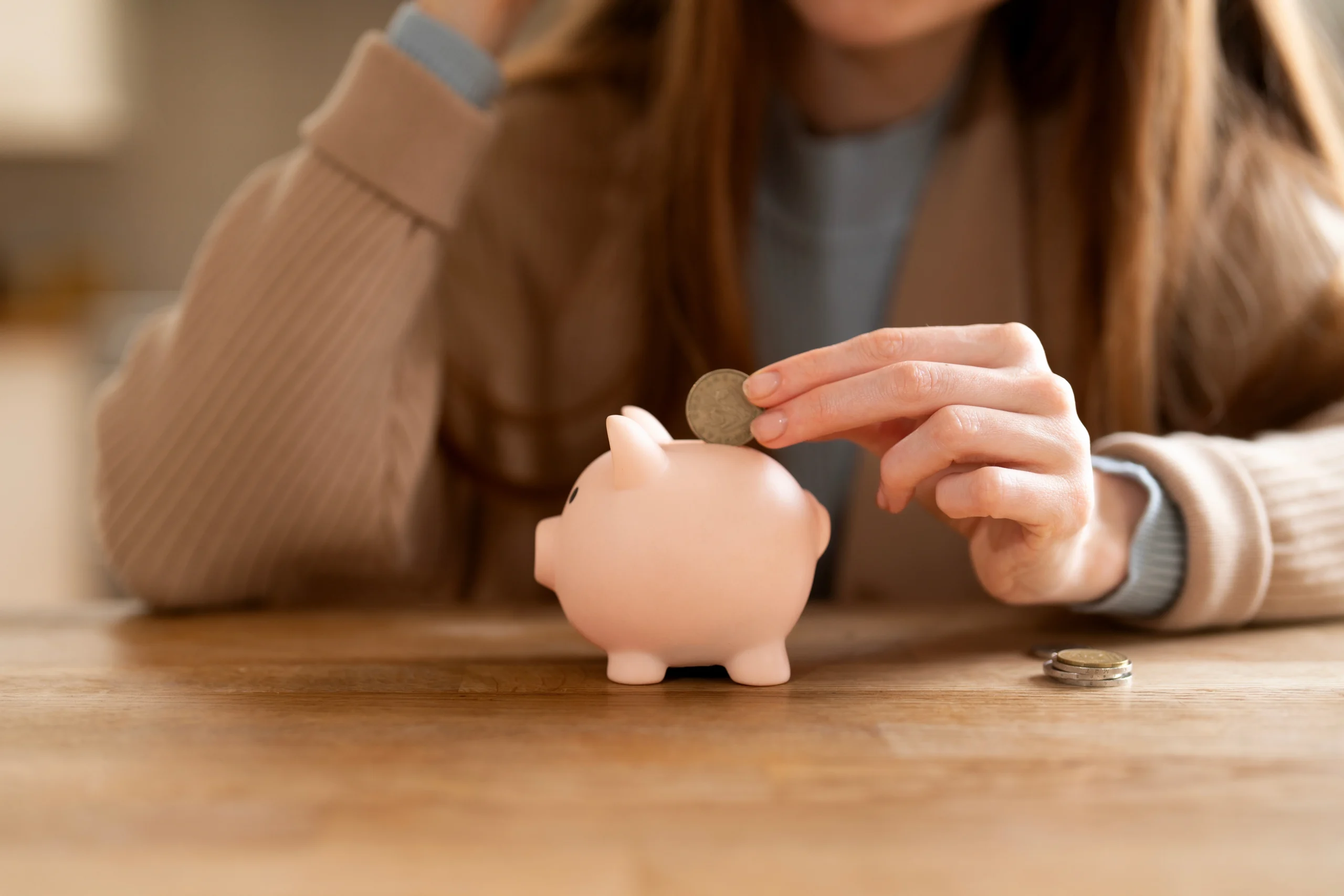Close up of a woman's hands putting a coin into a small piggy bank