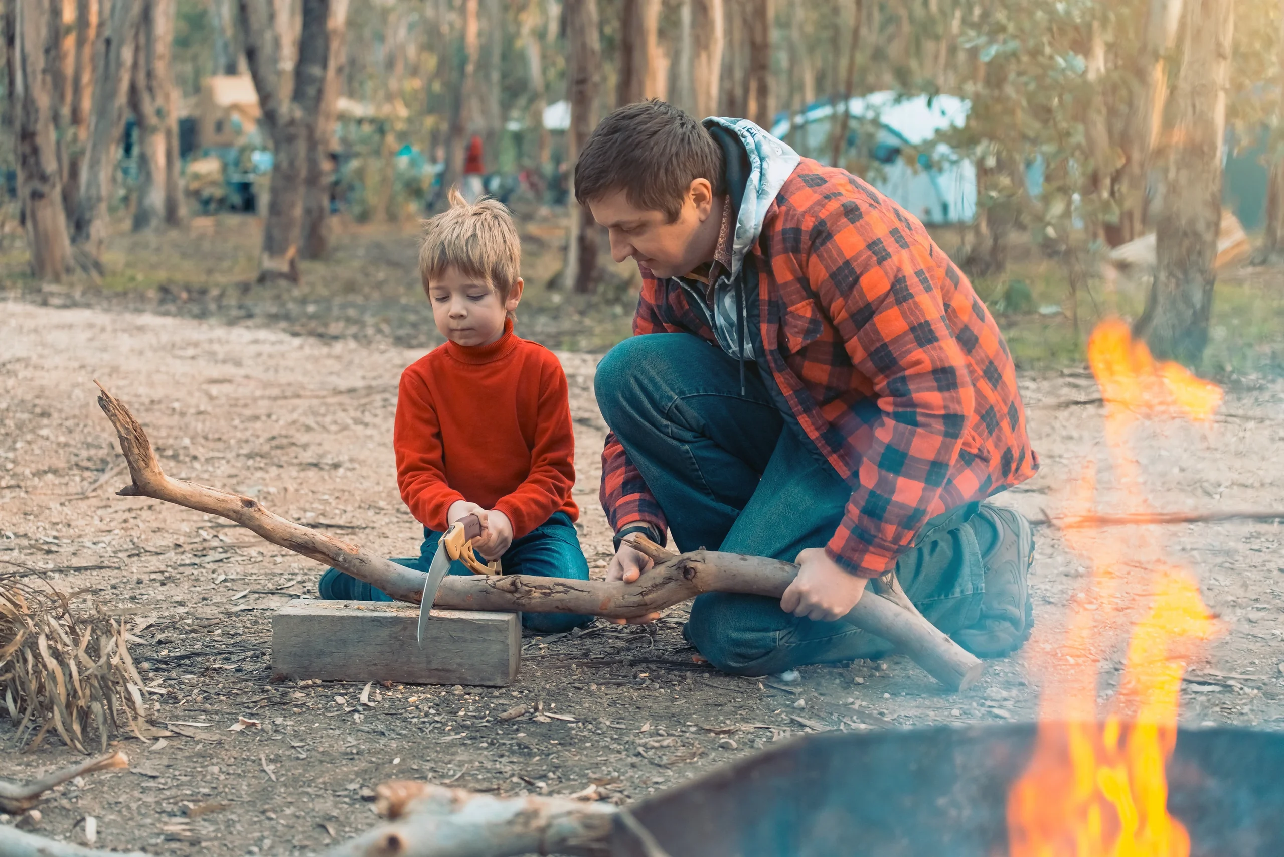Father shows son how to cut wood for fire while camping
