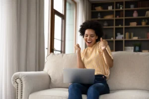 A woman grins and dances looking at her laptop, celebrating an instant approval loan