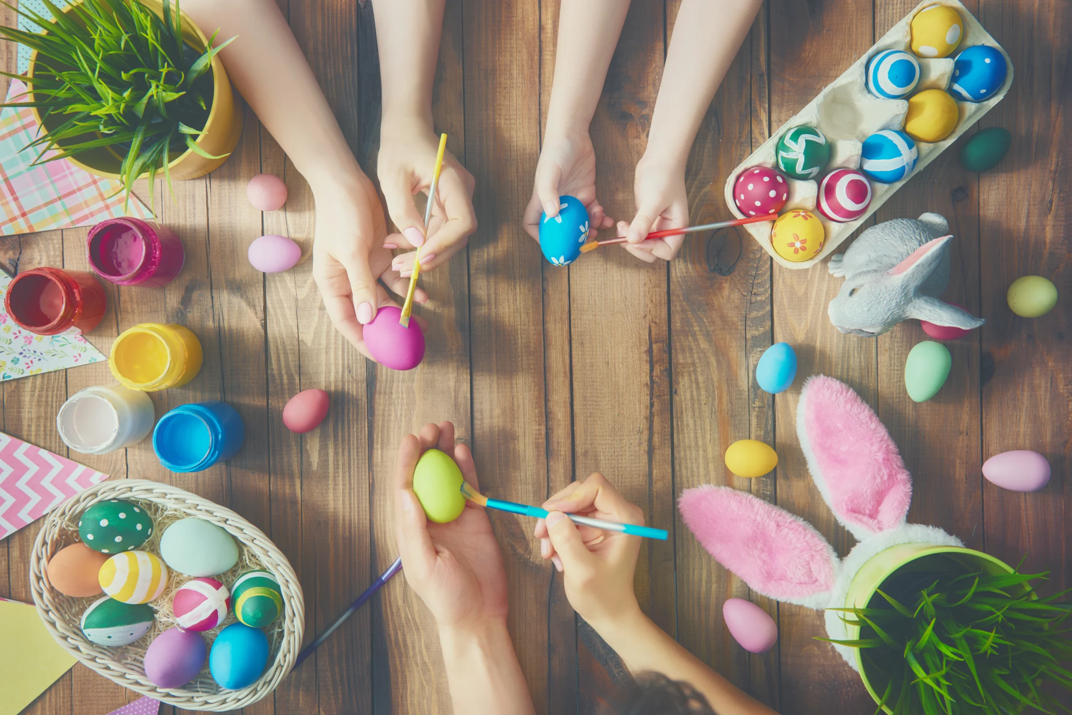 Close up of mum, dad, and child's hands painting easter eggs together at a table