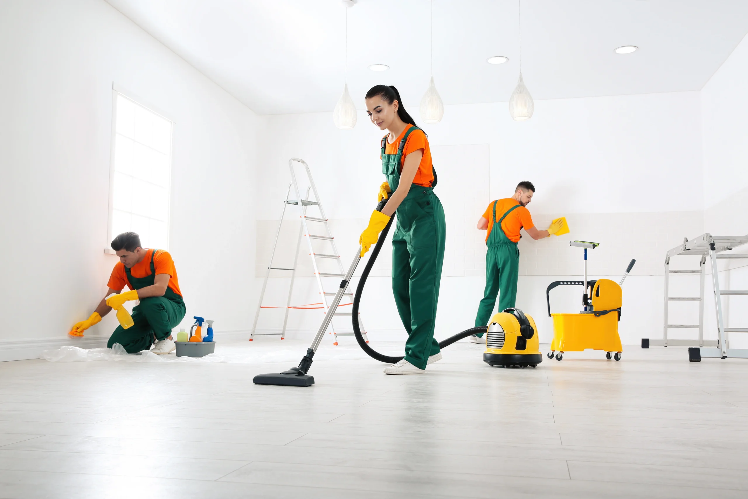 A team of cleaniners use vacuums and various clothes and sprays to clean a bright white space