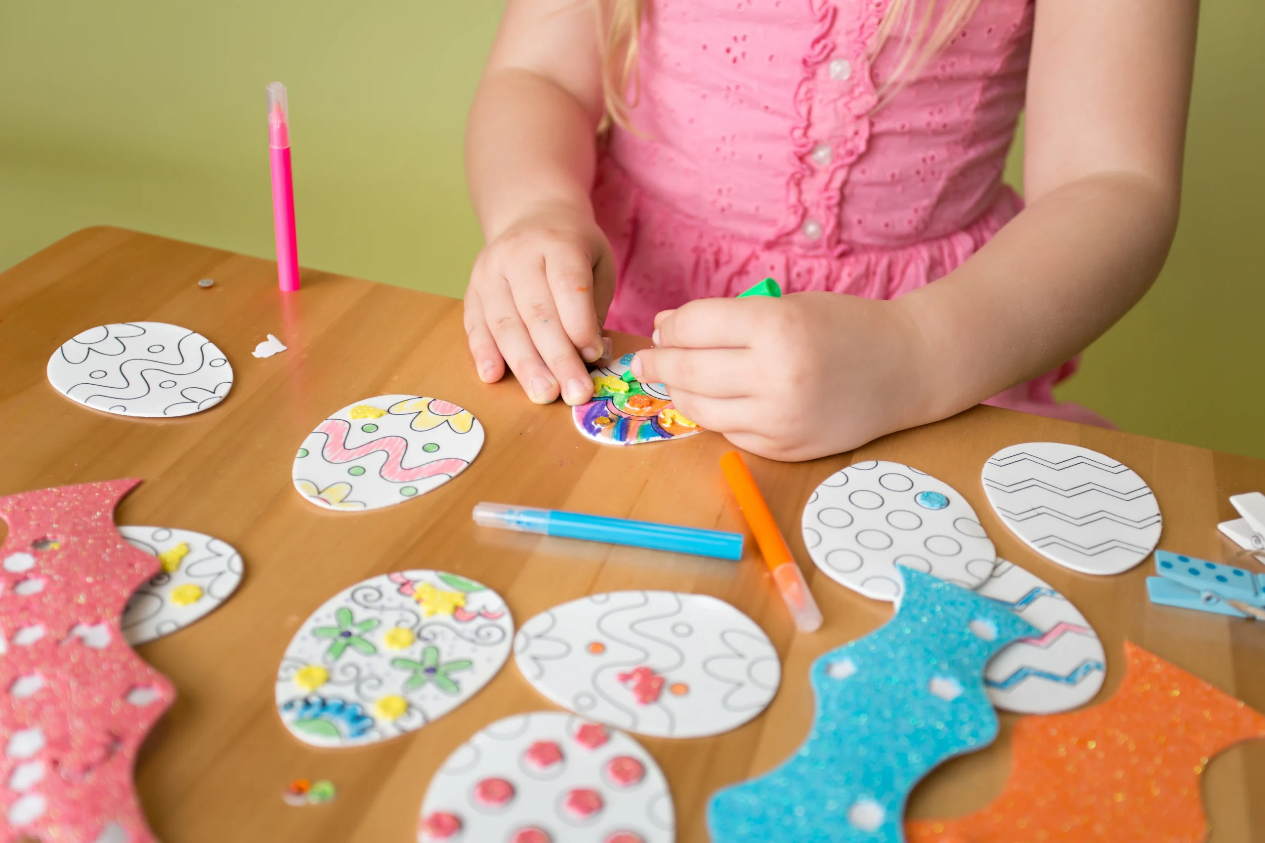 Close up of a child's hands while they colour in paper Easter eggs for a cheap Easter activity