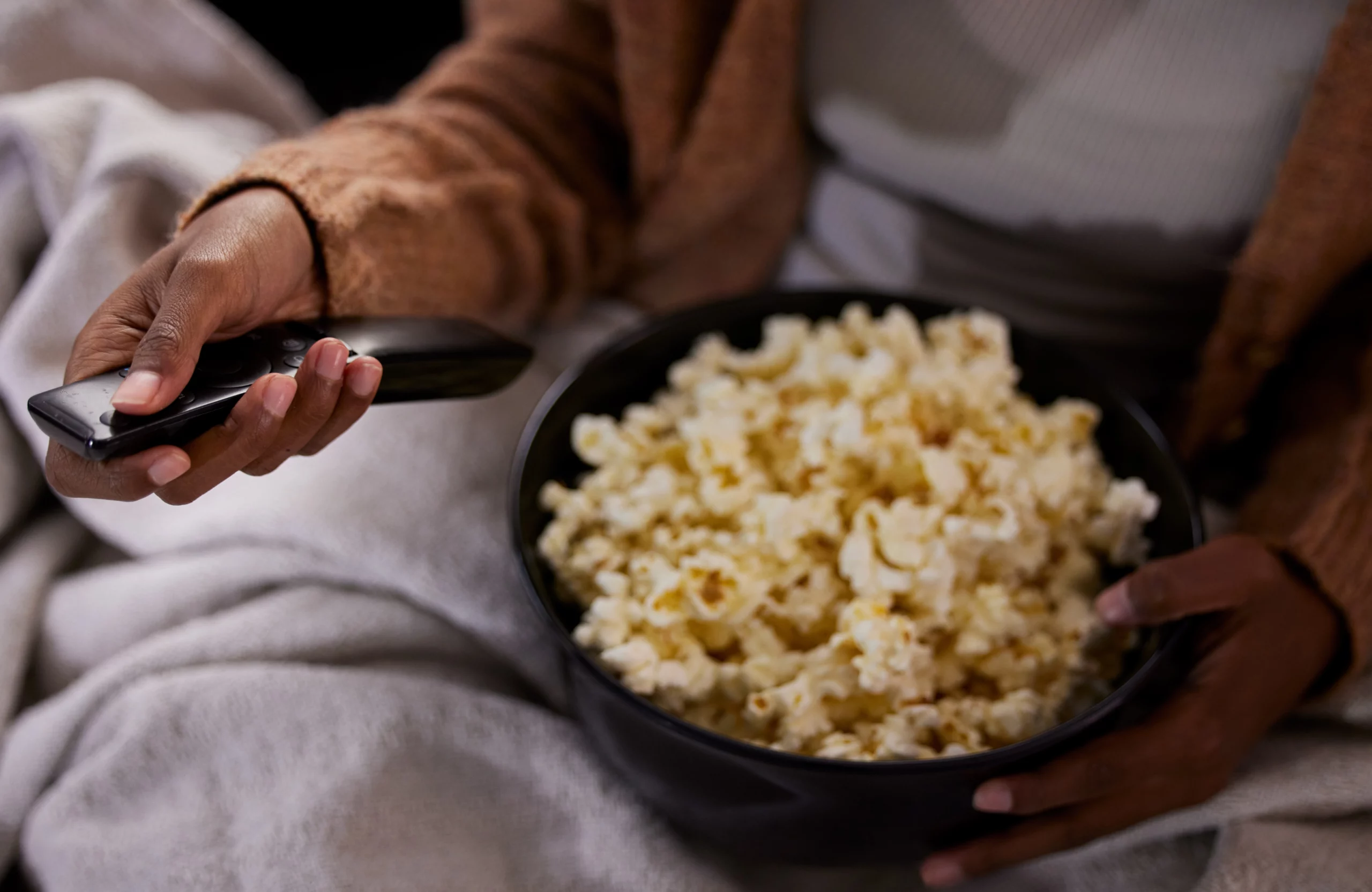 woman turning on TV snuggling up with a blanket and bowl of popcorn