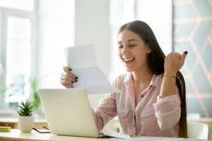 Woman reviewing financial documents while smiling at her laptop and learning whether a personal loan can improve her credit score.