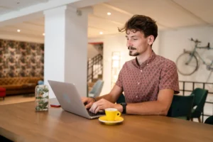 Man working on laptop at a table with a coffee, researching how to check credit score.