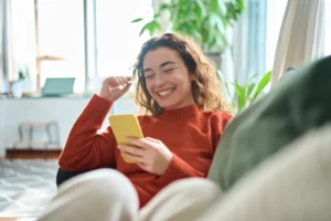 loans against cars; happy woman sitting on couch and using her phone